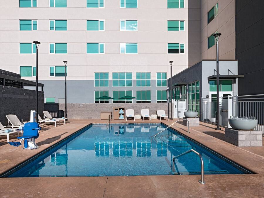 Piscina com espreguiçadeiras e guarda-sóis, rodeada por um edifício com várias janelas e design moderno.