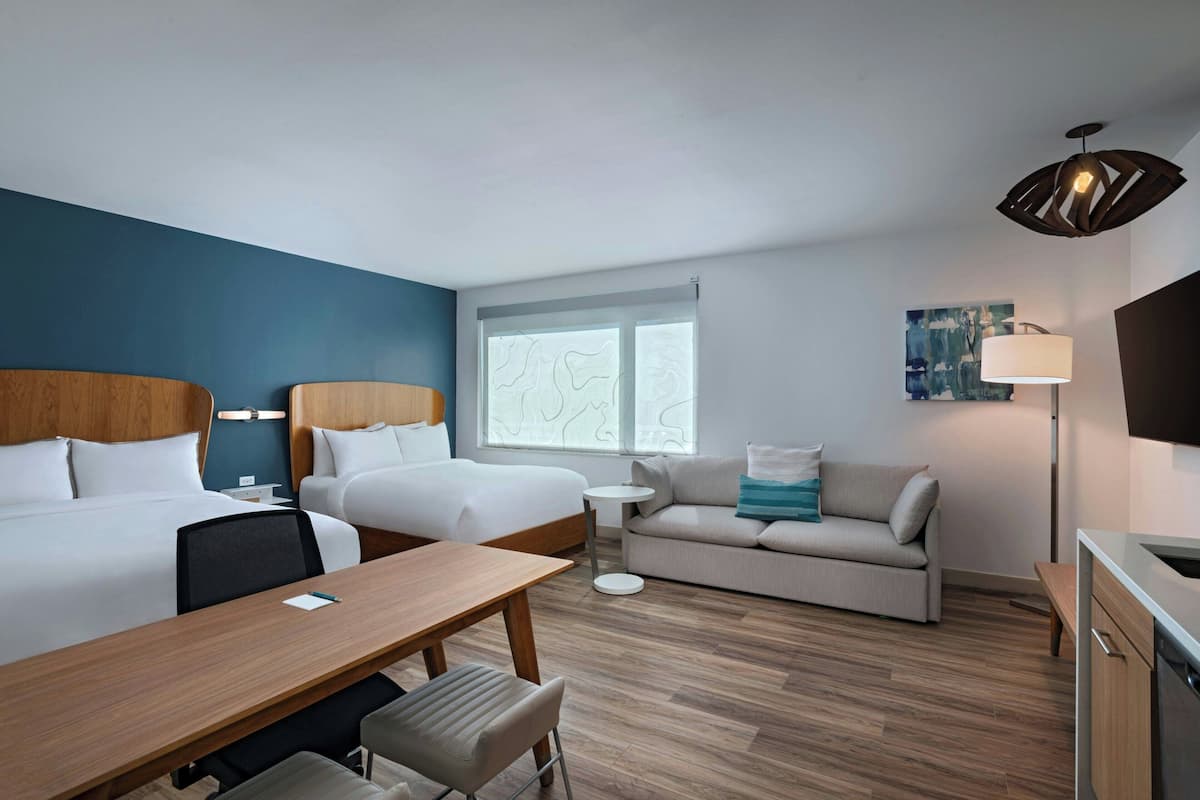 Une chambre d’hôtel avec deux lits, un canapé, une table à manger et une petite table ronde.