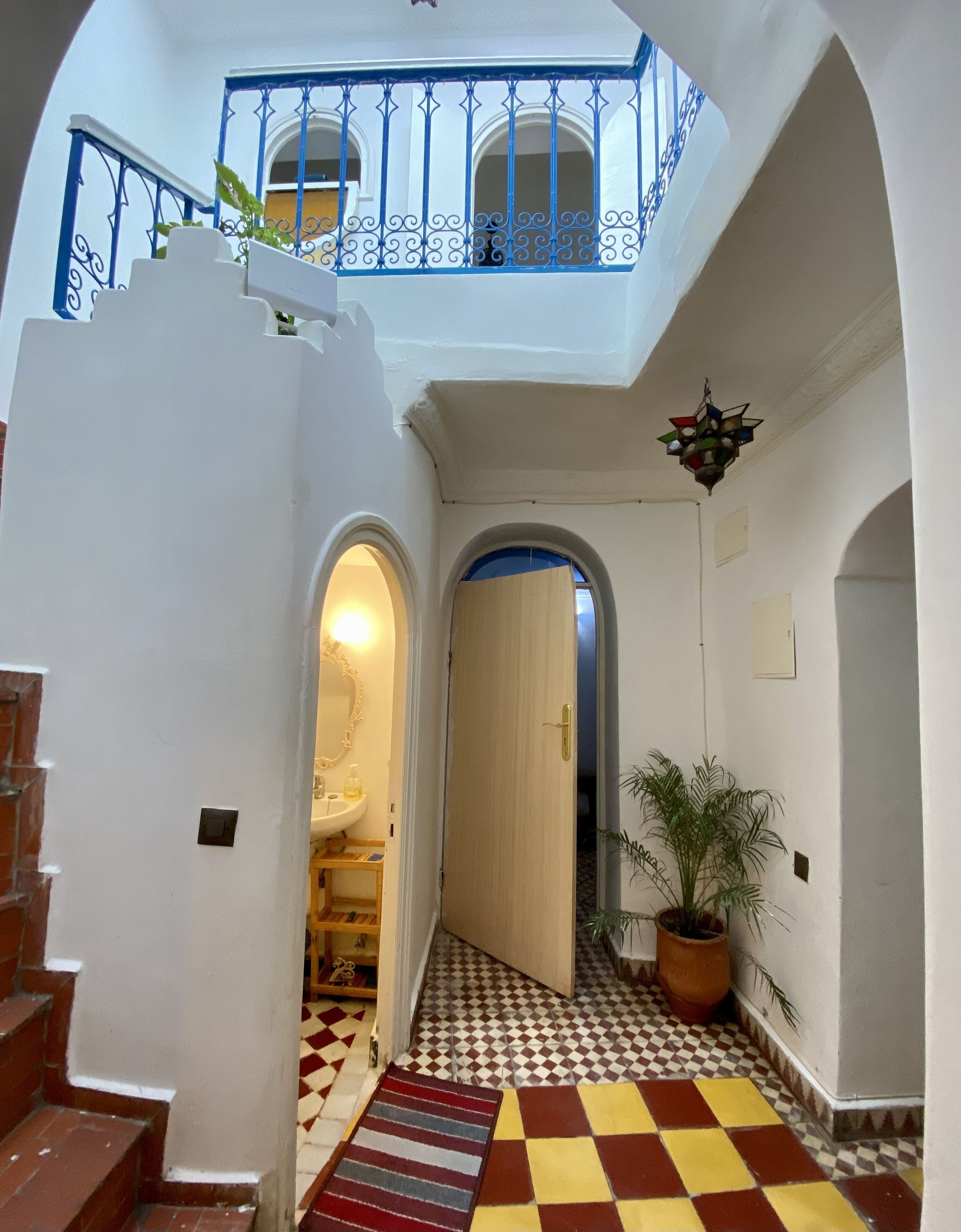 Un couloir avec un sol à carreaux, un escalier et un balcon doté de rampes bleues.