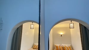 A mirrored view of a room with two beds, each with patterned bedding and pillows, a small round table, and a patterned rug. - Dar Coeur De Tanger (Tangier)