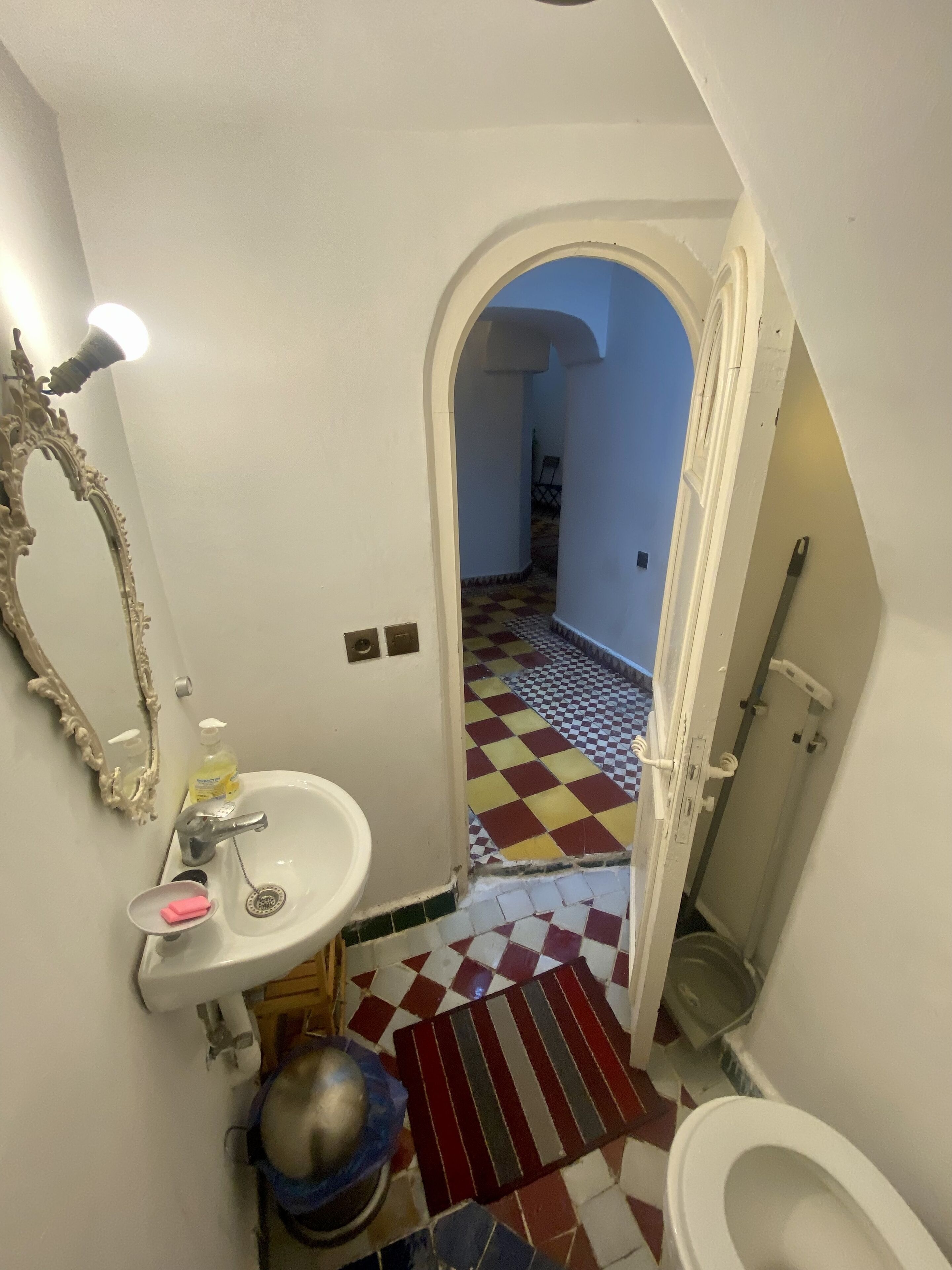 Une salle de bain avec un lavabo blanc, un miroir, des toilettes et un carrelage à motifs à carreaux.