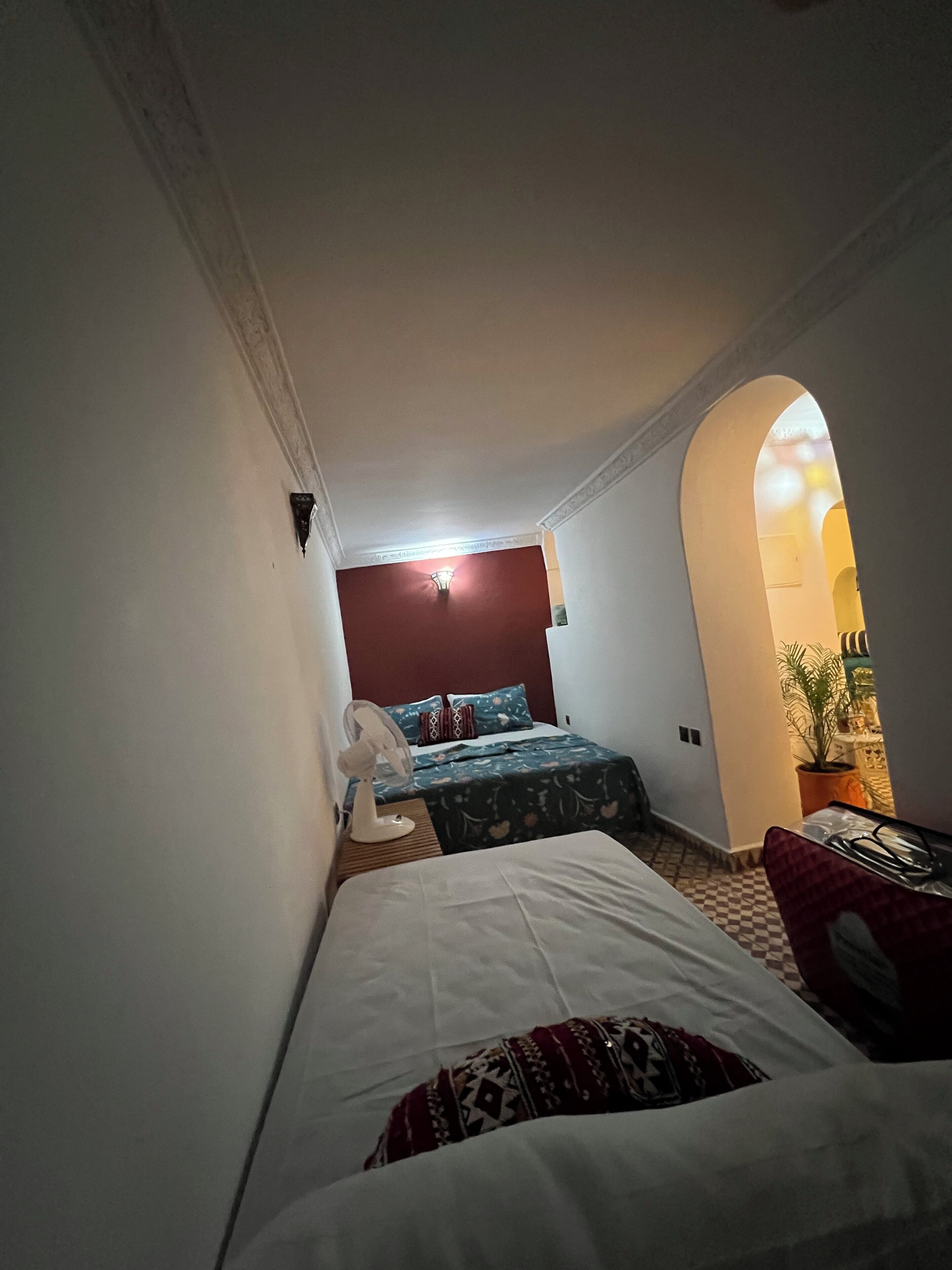 A narrow hallway leading to a bedroom with a bed, a fan, and a red wall.