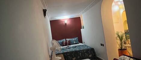 A narrow hallway leading to a bedroom with a bed, a fan, and a red wall.