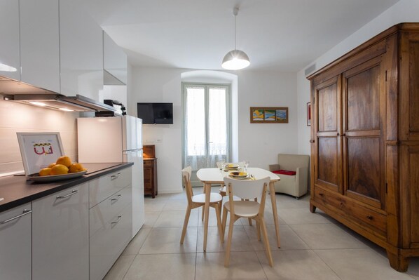 Una cocina moderna con armarios blancos, una mesa de comedor de madera con sillas, un mueble de madera grande y un televisor en la pared.