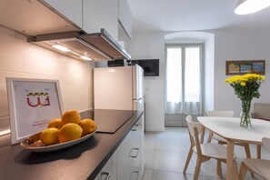 Una cocina moderna con un refrigerador de acero inoxidable, un cuenco de naranjas en la encimera y un comedor con una mesa y sillas blancas.