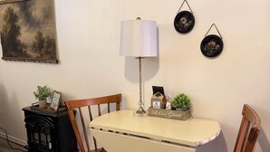 A dining area with a round table, four wooden chairs, a small black stove, a lamp, and wall decorations.