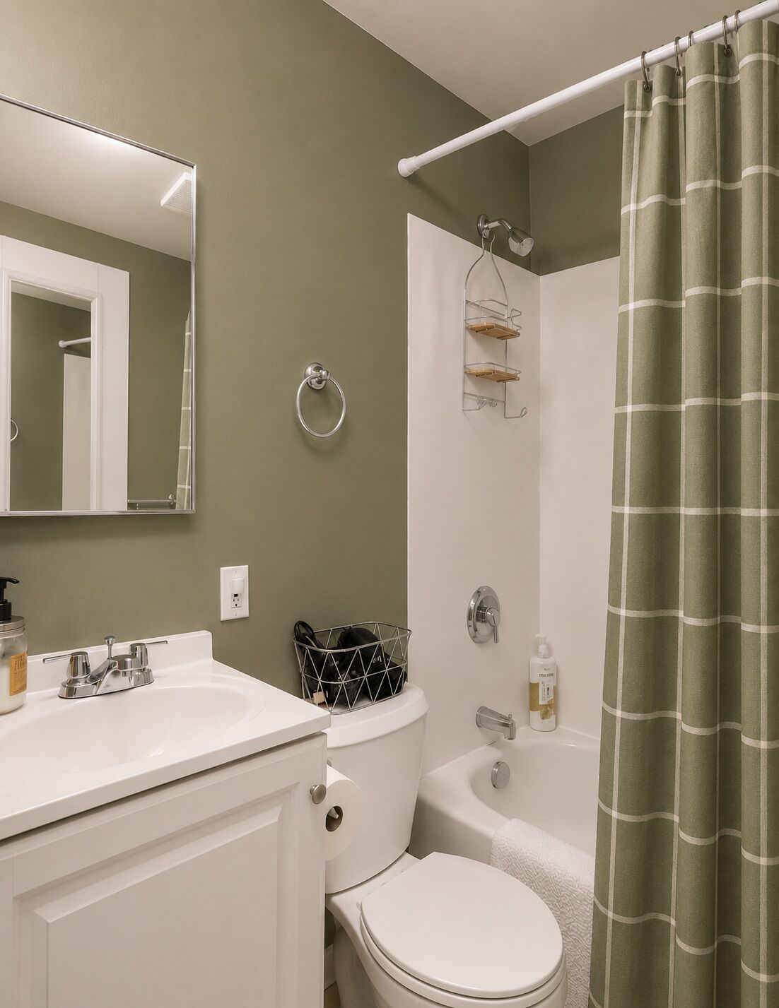 Une salle de bain avec un lavabo, des toilettes et une baignoire, tous de couleur blanche. On y trouve également un porte-serviettes, un rideau de douche et un miroir.