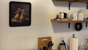 A kitchen with a stove, a cutting board, a coffee maker, and a shelf with glassware and dishes.