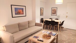 En stue med en beige sofa, et sofabord med blade og snacks, samt et spiseområde med et bord og stole.