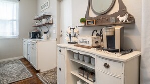 Una cocina con armarios blancos, una cafetera, un estante con utensilios de cocina y un cartel que dice 'Farmers Market'.