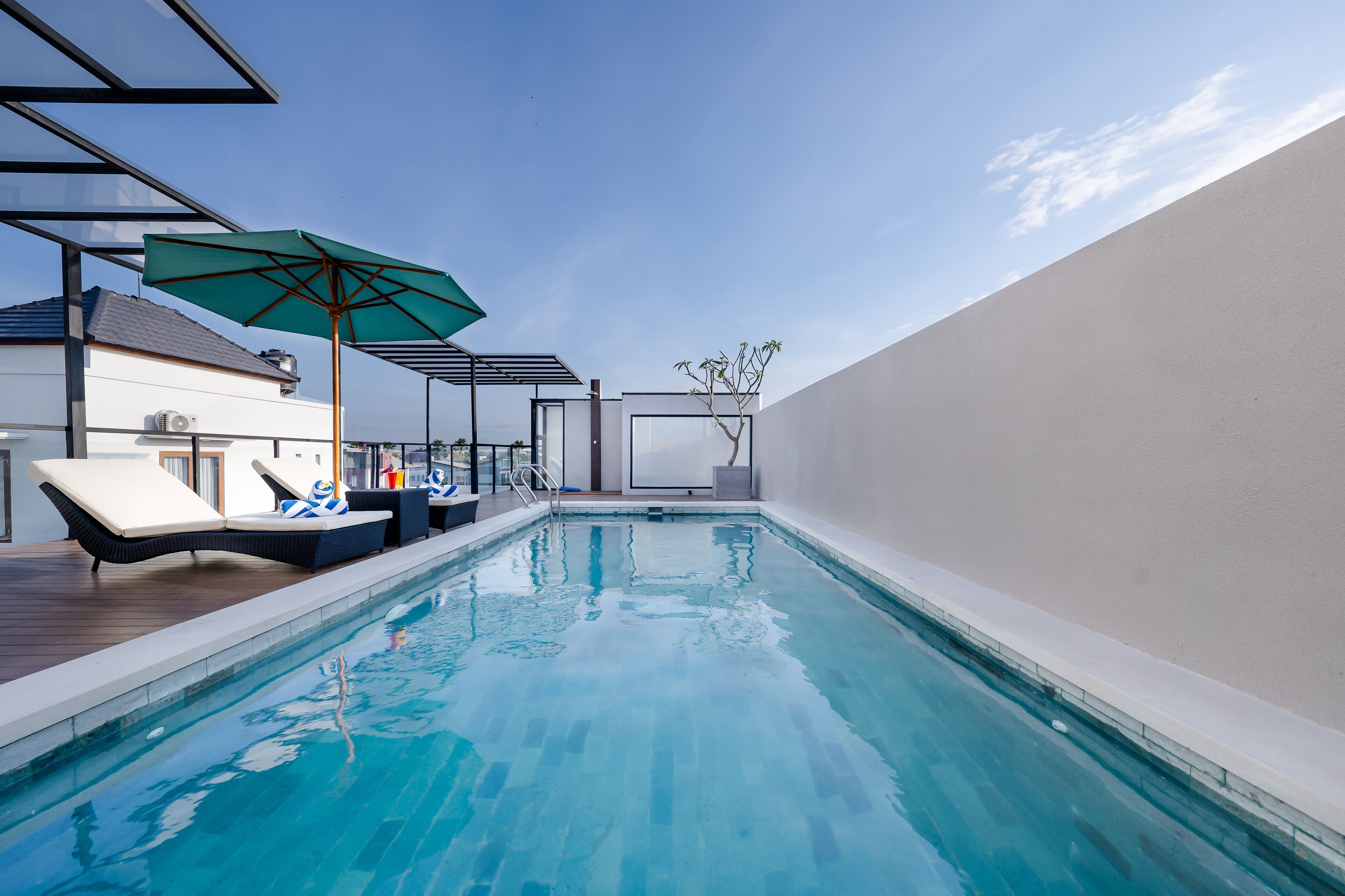 A swimming pool with lounge chairs and an umbrella, surrounded by a modern building with a white exterior.