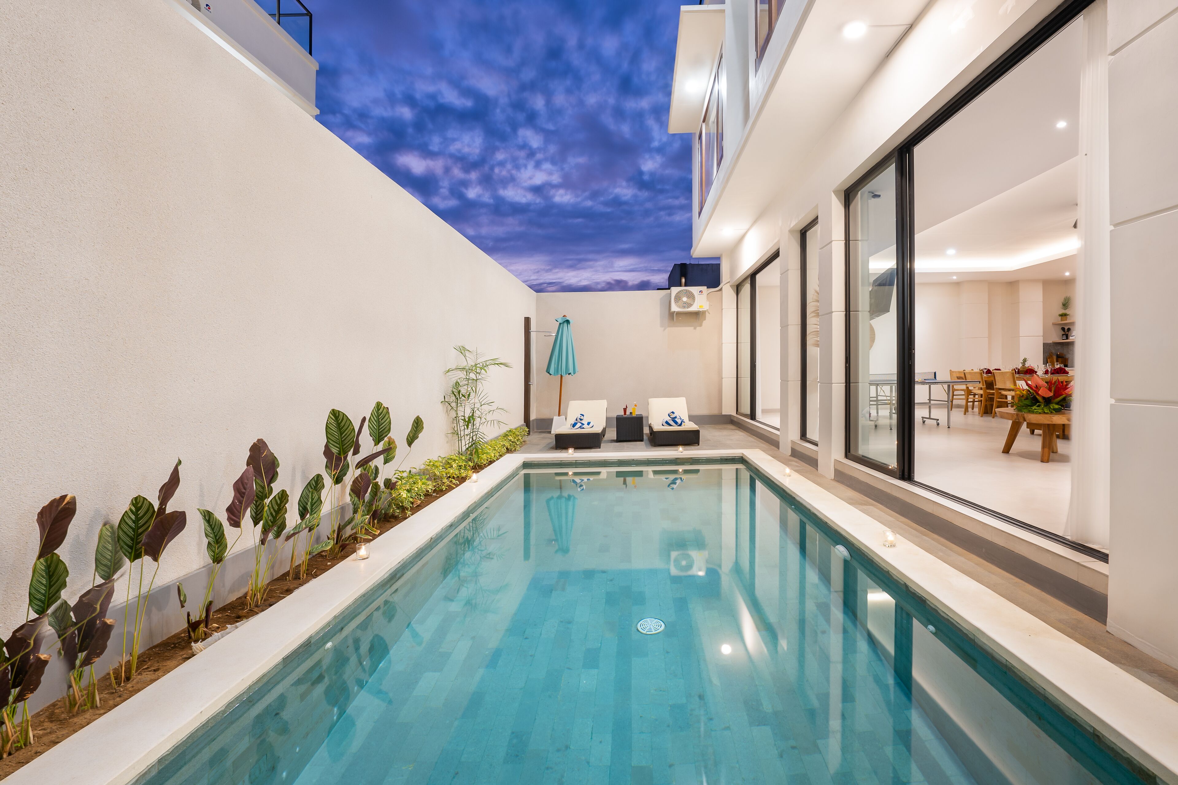 A modern indoor pool with clear blue water, surrounded by a white wall and a balcony.