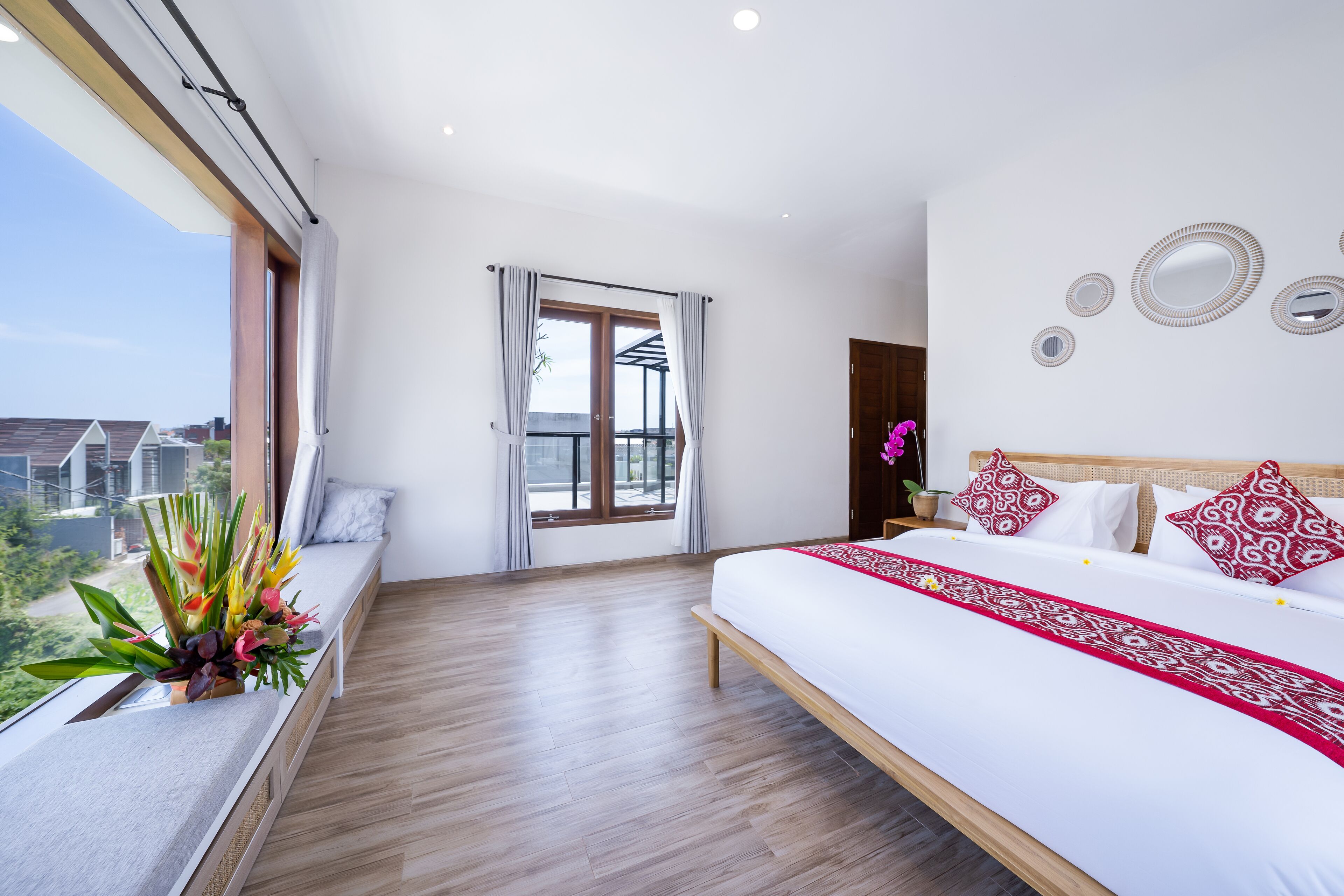 A bedroom with a large bed, a window with curtains, a balcony, and a view of buildings.