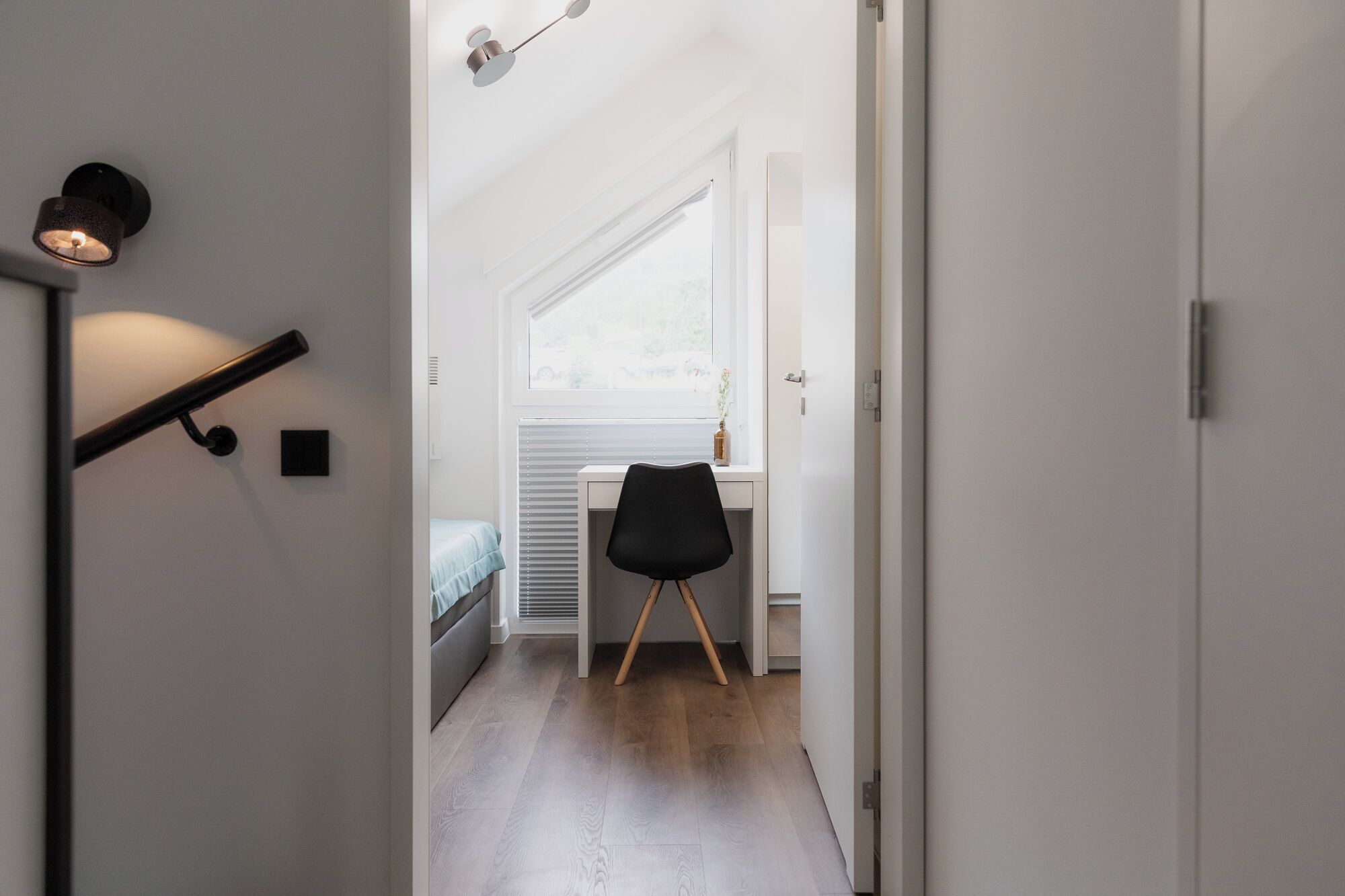 Un pasillo estrecho que conduce a un dormitorio con cama, escritorio y silla.
