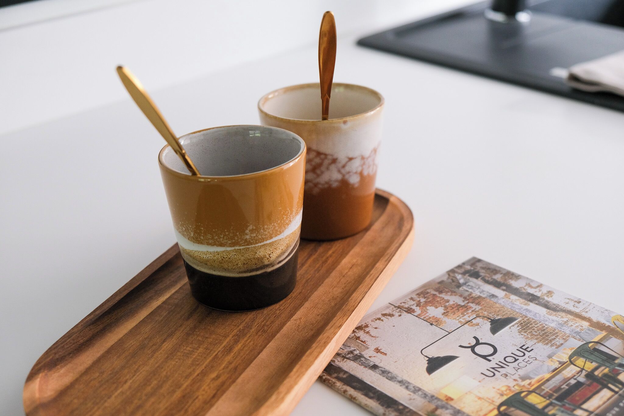 Two cups of coffee on a wooden tray with a magazine featuring 'Unique Places' on a table.