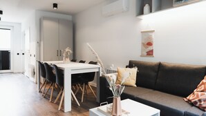 A modern living room with a grey sofa, a white coffee table, and a dining area with a white table and black chairs.