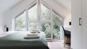A bedroom with a large window, a bed with a green bedspread, and a desk with a chair.