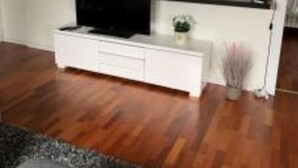 A modern living room with a flat-screen TV on a white entertainment unit, wooden flooring, and a grey sofa.