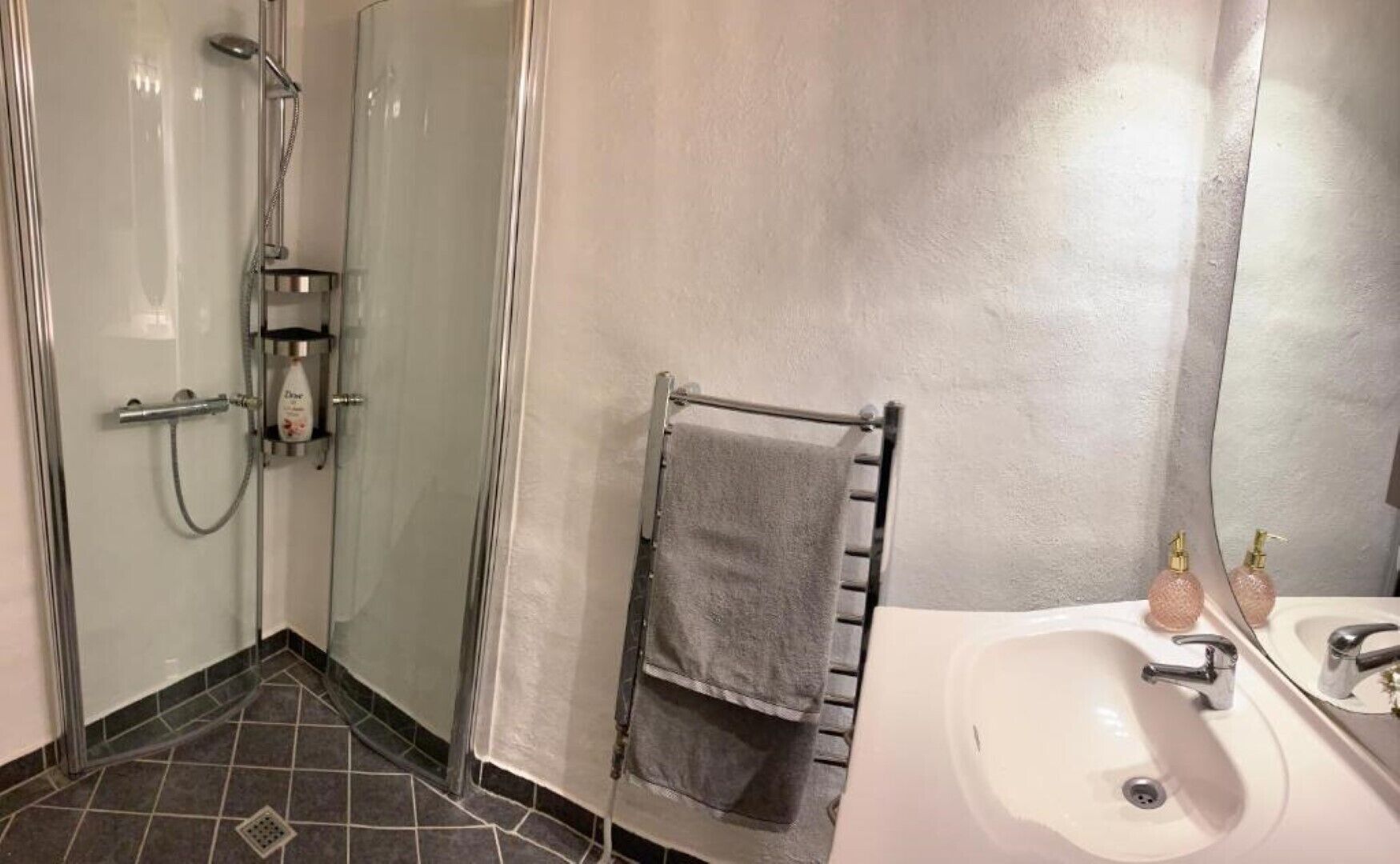 A bathroom with a glass-enclosed shower, a towel rack with a towel, and a sink with soap dispensers.