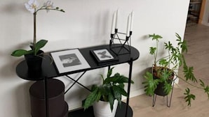 A modern room with a round mirror, a black console table with framed pictures, and potted plants.