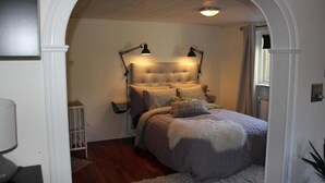 A bedroom with a tufted headboard, two bedside lamps, a bed with a fluffy blanket, and a small bedside table.