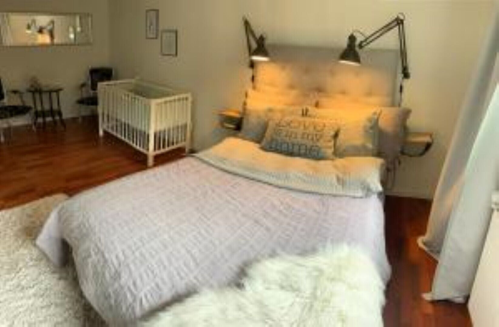 A bedroom with a bed, a crib, a nightstand, and a lamp.