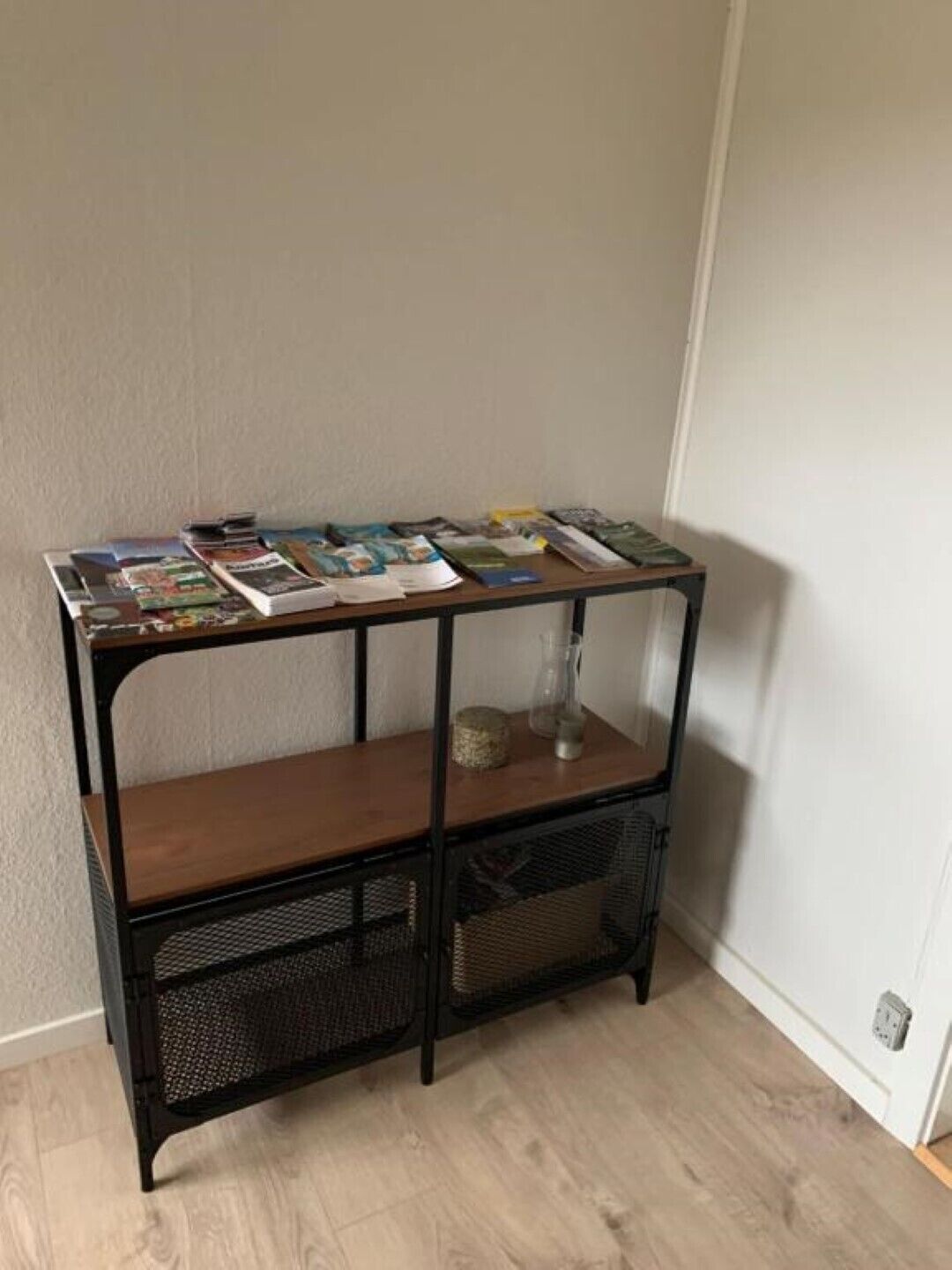 Ein Nachttisch aus Metall und Holz mit Zeitschriften und einer Vase.