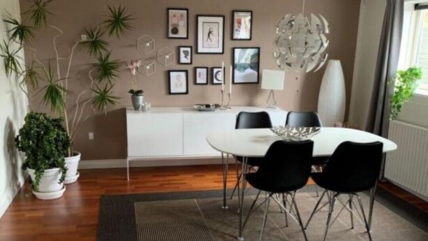 A dining area with a round table, black chairs, a white cabinet, and framed pictures on the wall.