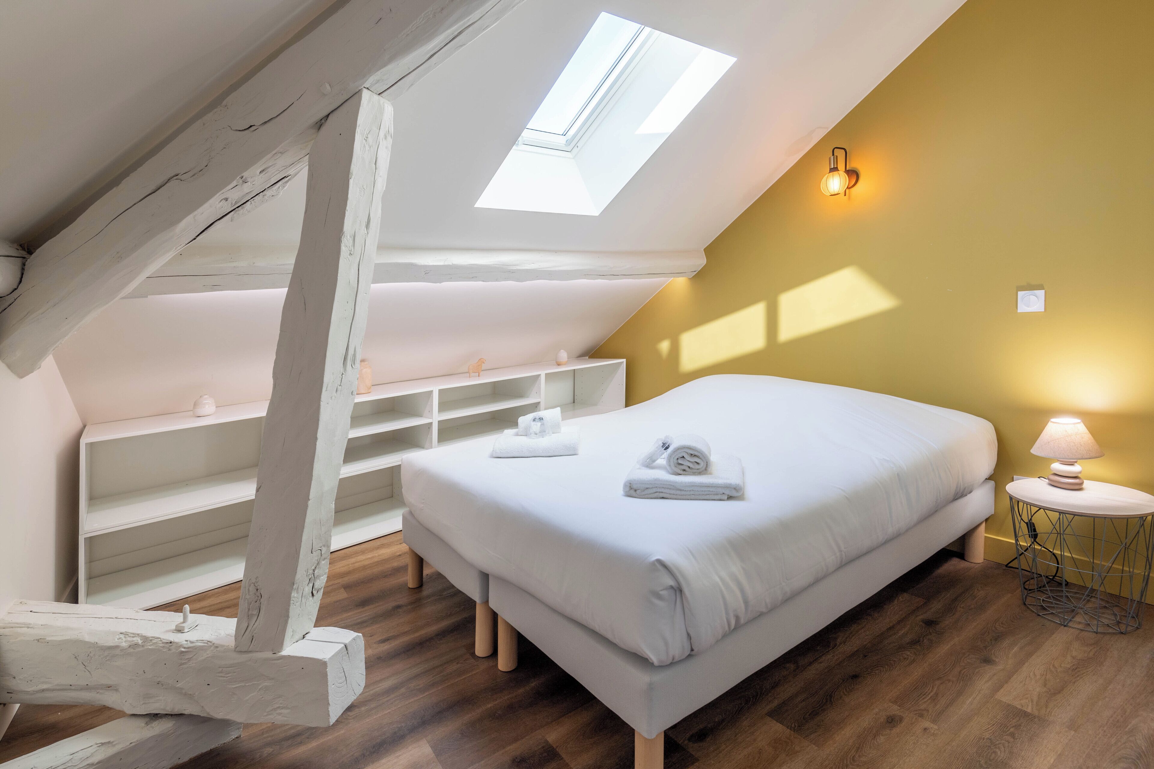 Ein Schlafzimmer mit Oberlicht, einem Bett mit Handtüchern, einer Nachttischlampe und Holzboden.