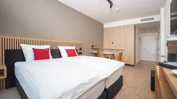A modern hotel room with a large bed, a desk, and a wardrobe.