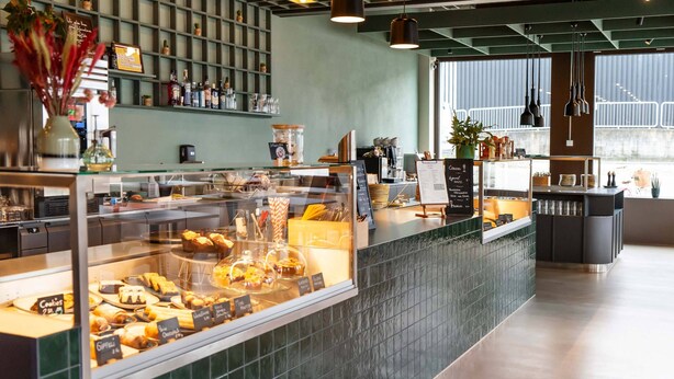 A bakery counter with various baked goods on display, a coffee machine, and a menu board.
