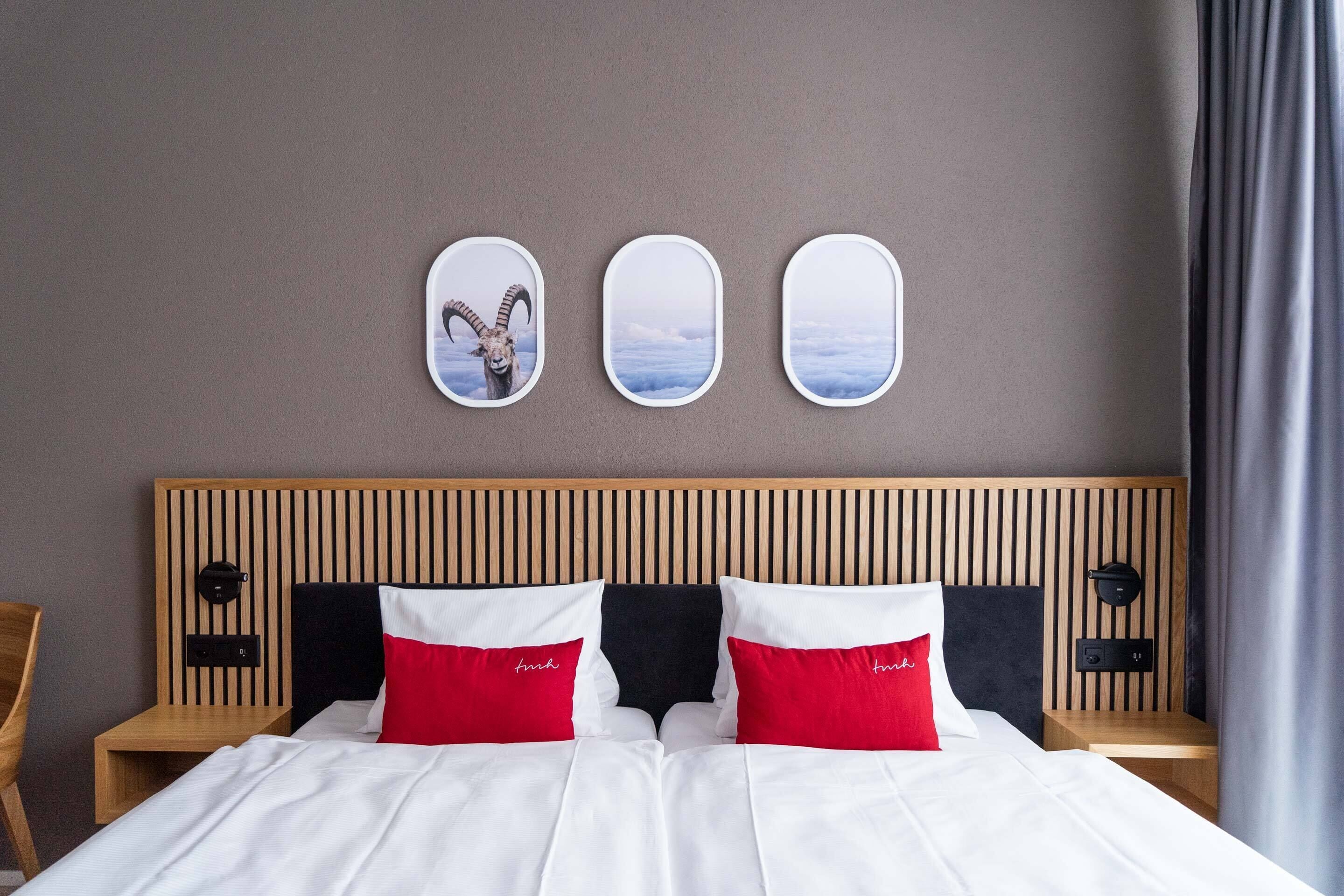 Une chambre d’hôtel avec une tête de lit en bois, un lit avec une literie blanche et rouge, et trois miroirs muraux.