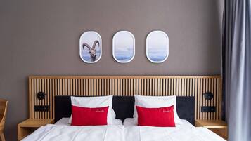 Une chambre d’hôtel avec une tête de lit en bois, un lit avec une literie blanche et rouge, et trois miroirs muraux.