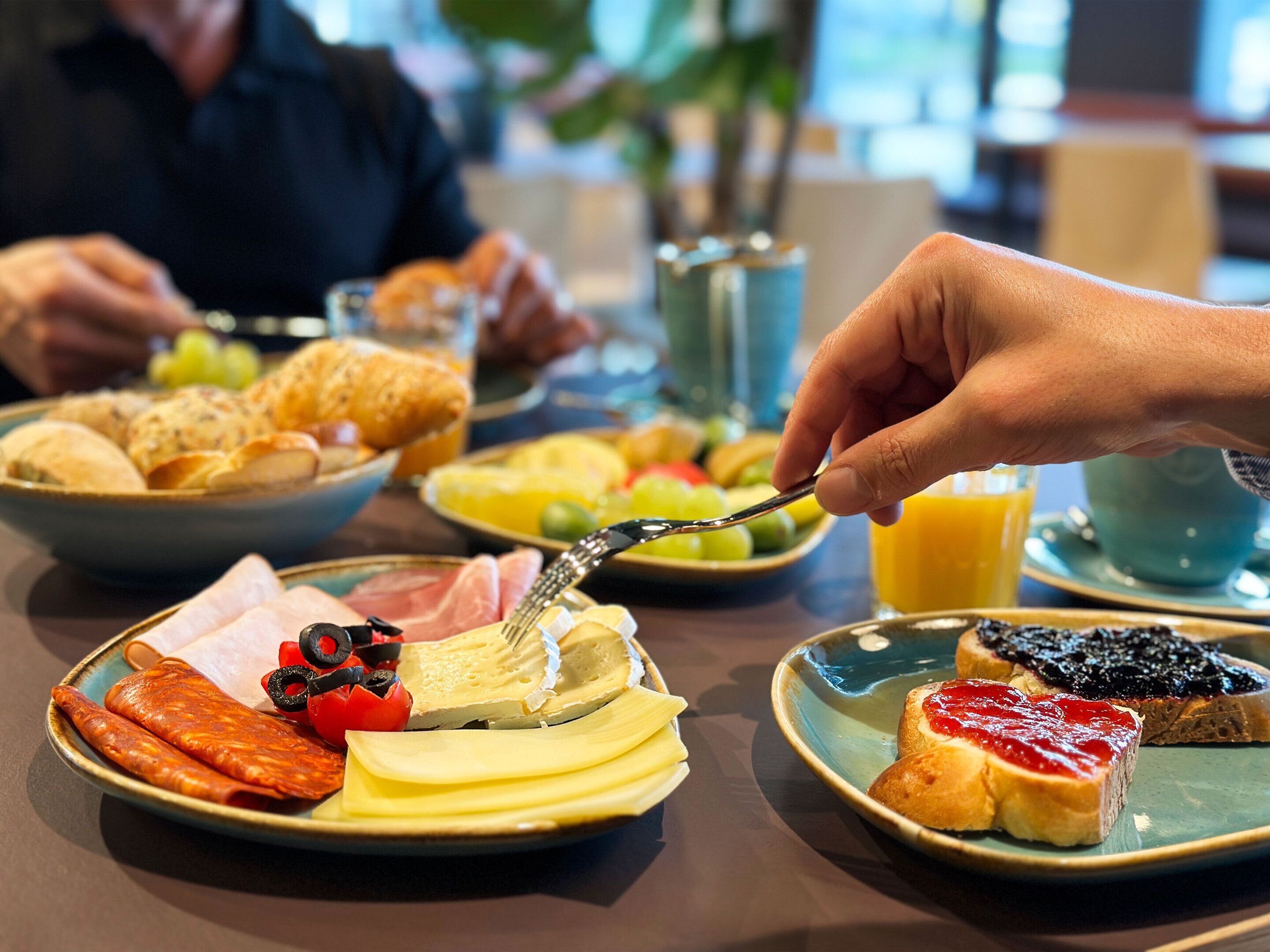 Desayuno servido con platos de comida, incluyendo tostadas con mermelada, queso y tomates, junto con un vaso de jugo de naranja.