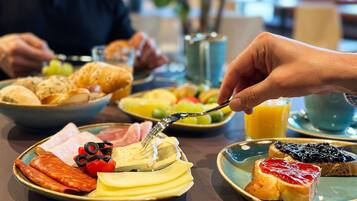 Desayuno servido con platos de comida, incluyendo tostadas con mermelada, queso y tomates, junto con un vaso de jugo de naranja.