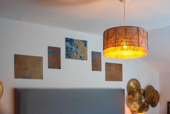 Une pièce avec une lampe suspendue, un lit et quatre œuvres d’art encadrées accrochées au mur.