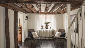 A room with exposed wooden beams, a dark wooden floor, two wicker chairs with cushions, a small table with a plant, and a white door leading to another room. - Lovely 3-bed House in West Malling, Kent (West Malling)