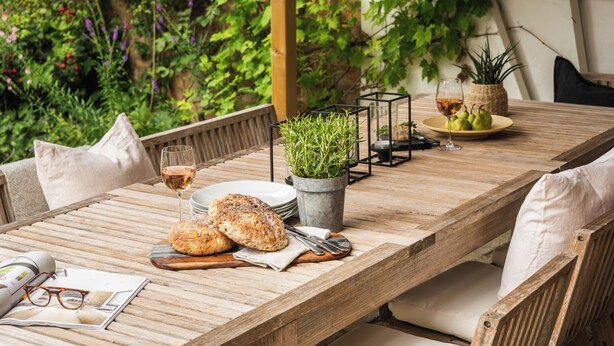 A wooden dining table set with plates, glasses, a bread basket, and a potted plant. - Lovely 3-bed House in West Malling, Kent (West Malling)