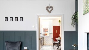 Un pasillo con una butaca tapizada en gris oscuro, una mesita con libros y una decoración con forma de corazón en la pared.