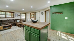 Uma sala de estar acolhedora com um sofá seccional, uma mesa de centro de madeira e uma ilha de cozinha verde com pia.