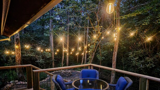 Um deck externo com móveis de vime e luzes de corda, rodeado por árvores.