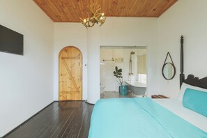 A bedroom with a wooden ceiling, a bed with a teal bedspread, a wooden door, a bathroom with a bathtub, and a mirror. - Da Lat Lacasa (Xuan Huong - Da Lat)