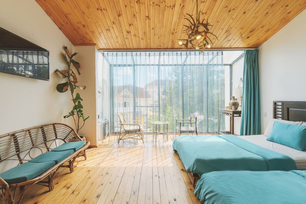 A room with a wooden ceiling, a bed with teal bedding, a wicker sofa, and a small table with chairs.