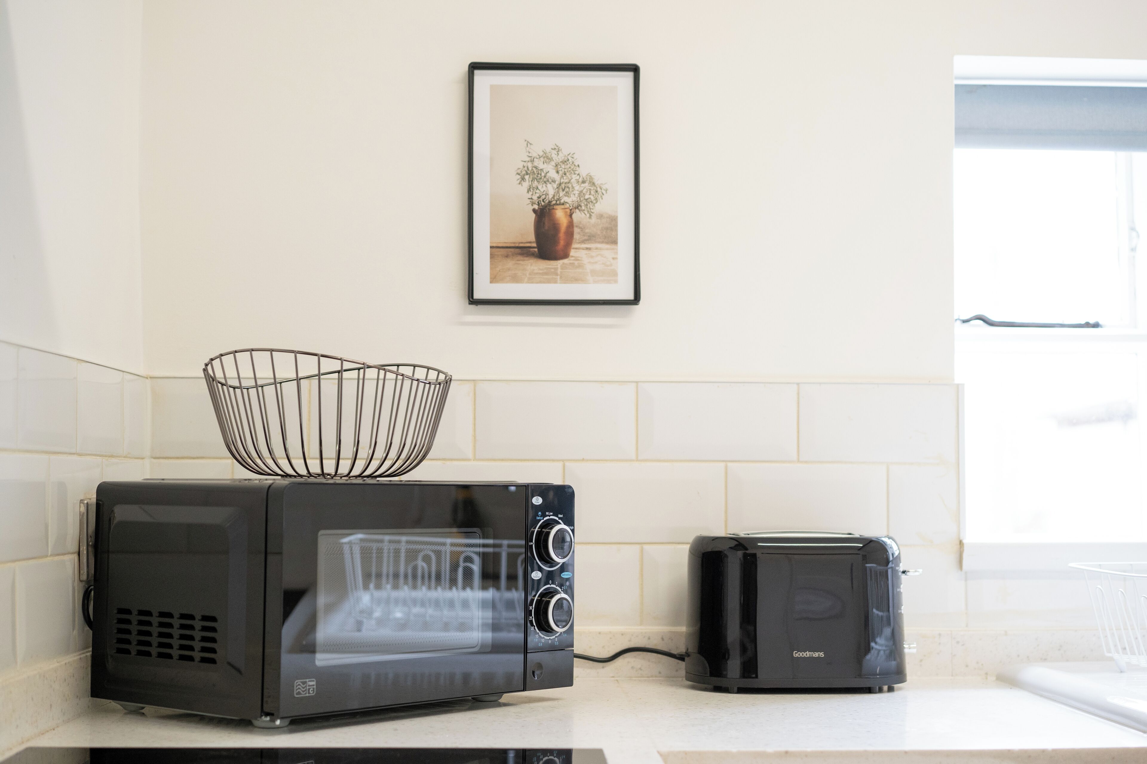 Una cucina con un forno a microonde nero, un tostapane e un quadro appeso al muro.