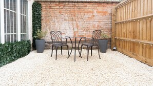Un patio con pared de ladrillo, valla de madera y una mesa con sillas.