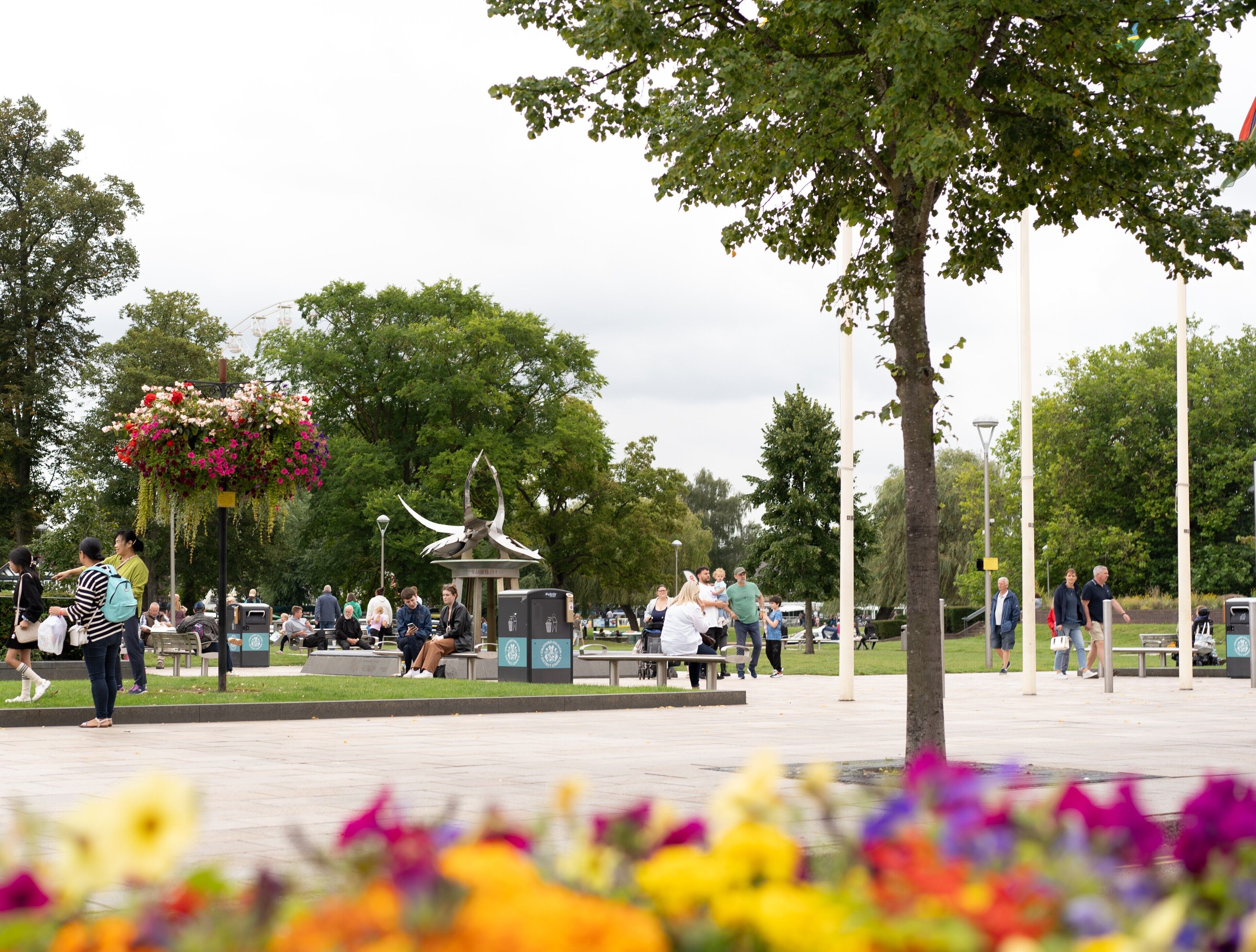Un parque público con bancos, una escultura y gente caminando.