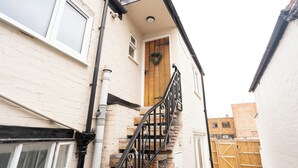 Una escalera estrecha conduce a una puerta de madera adornada con un adorno, un edificio de ladrillo blanco y un portón de madera al fondo.