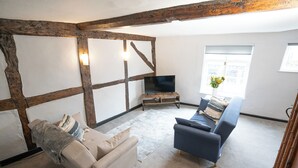 Sala de estar con vigas de madera a la vista, un sofá color beige, un sofá azul, un televisor de pantalla plana sobre un soporte de madera y una ventana con vista a edificios.