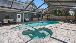 Ein Pool mit geometrischem Muster, umgeben von einer überdachten Terrasse mit Sitzgelegenheiten und einem kleinen Tisch.