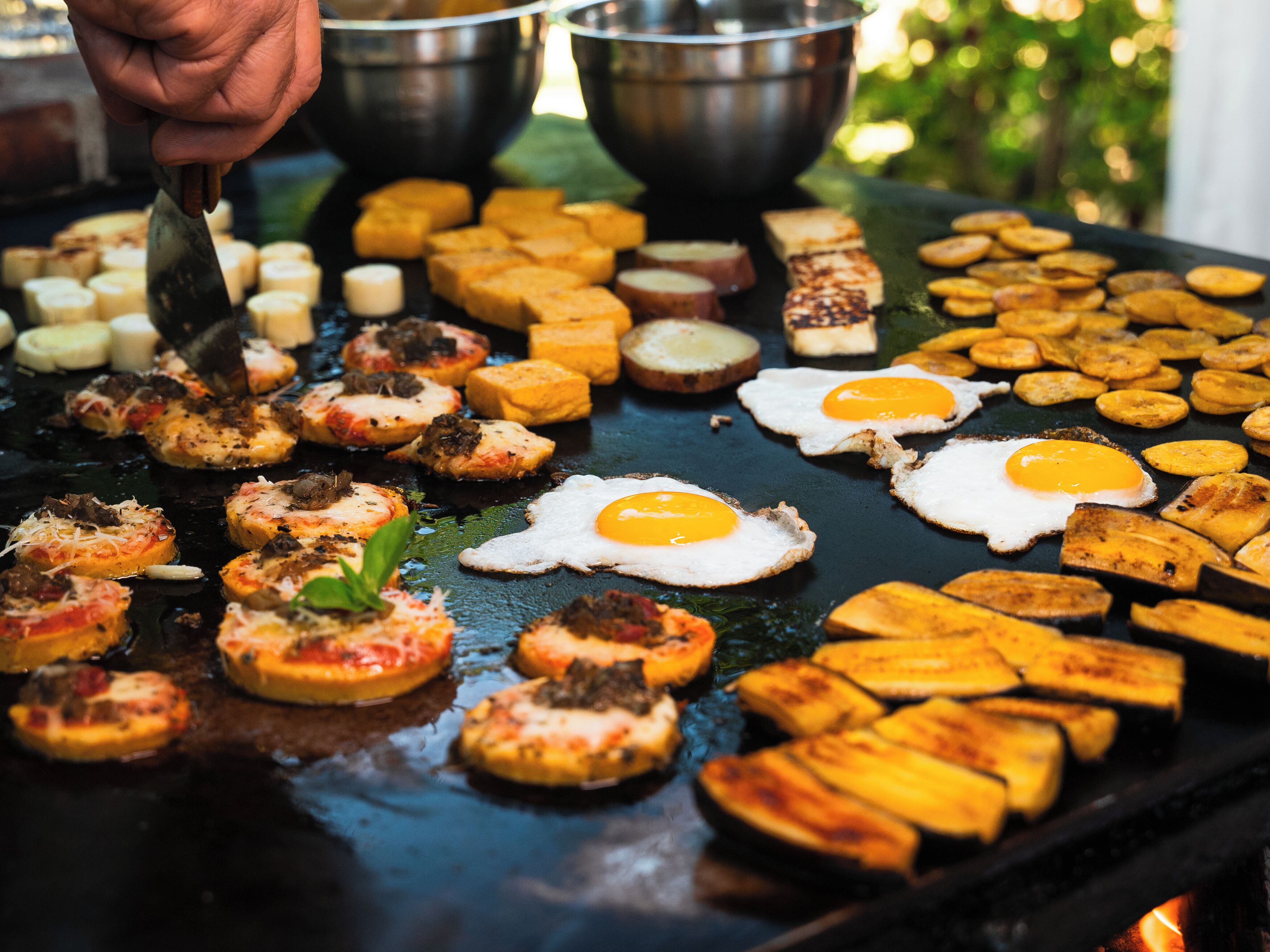 Une variété d’aliments grillés sur une surface de cuisson plane, notamment des œufs, de la viande et des légumes.